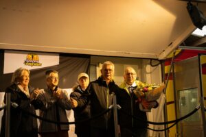 Sur la scène, un groupe d'organisateurs et d'élus applaudit, l'un d'eux tenant un bouquet.