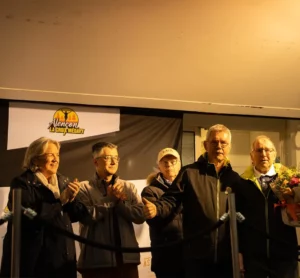 Sur la scène, un groupe d'organisateurs et d'élus applaudit, l'un d'eux tenant un bouquet.